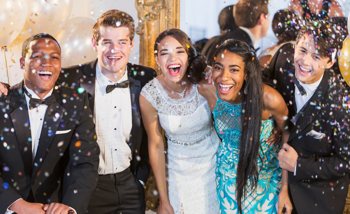 group of teens at prom smiling at camera with confetti falling around them